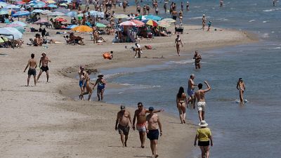 Playa concurrida en d�a soleado, llena de gente disfrutando del mar y la arena bajo sombrillas de colores. Escena de verano con actividad y alegr�a.