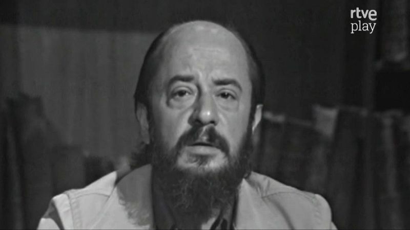 Plano medio corto de Fernando Jiménez del Oso, con calvicie, barba y bigote, mirando al frente. Logo de "rtve play" en la esquina superior derecha. Fondo oscuro y desenfocado.
