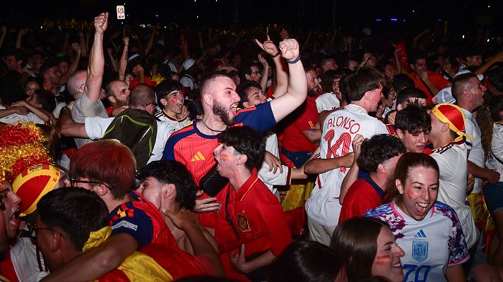 Aficionados españoles celebran eufóricamente una victoria nocturna, luciendo camisetas de la selección y caras pintadas. Se aprecian gritos y puños alzados en señal de júbilo.