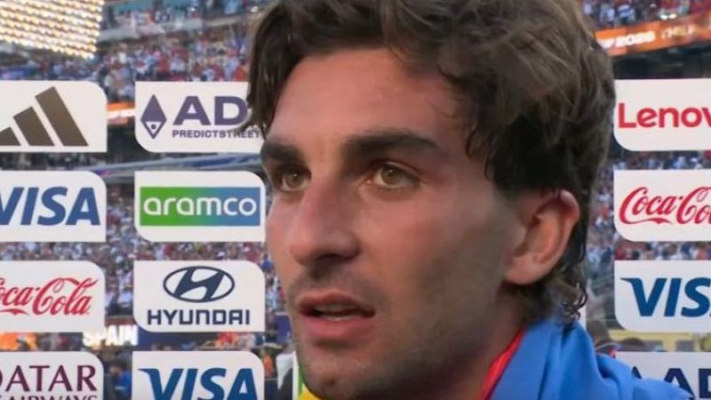 Primer plano de Ferran Torres, futbolista español, con expresión seria. Viste equipación azul y roja. Fondo de estadio y patrocinadores como Adidas, VISA, Coca-Cola.