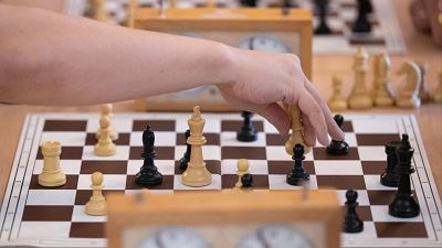 Primer plano de una mano sosteniendo una reina blanca sobre un tablero de ajedrez con notaci�n algebraica, en una partida cronometrada.