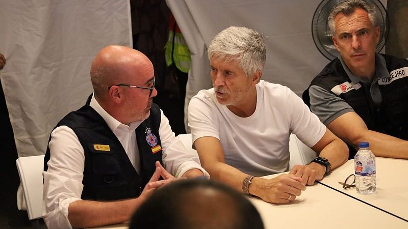 Fernando Grande-Marlaska, Ministro del Interior, se reúne con dos hombres en un puesto de mando avanzado. Uno viste chaleco de Protección Civil, el otro lleva "CONSEJERO" en su chaleco.