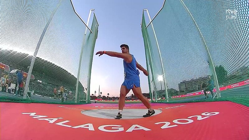 Atleta masculino lanzando en una pista de atletismo con "MÁLAGA 2026" en el suelo. Se observa la jaula de lanzamiento, gradas y el logo de TVE Play.