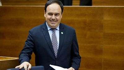 Primer plano de Juanfran P�rez Llorca, presidente de la Generalitat Valenciana, sonriendo y sosteniendo folios. Viste traje azul oscuro y camisa azul claro.
