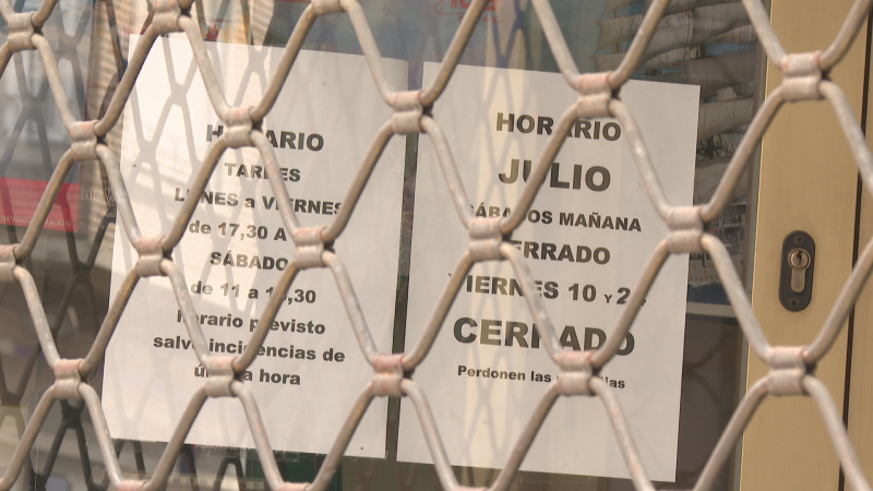 Entrada de un negocio cerrado con persiana metálica. Carteles informan horario habitual y cierre temporal en julio: Sábados mañana y viernes 10 y 2 cerrados. Perdonen las molestias.