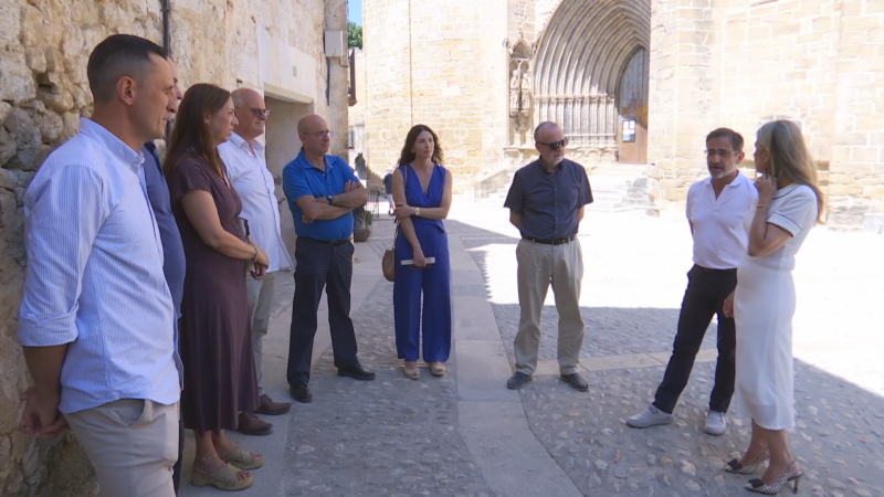 Ocho personas, entre ellas Mar Vaquero, Jorge Azcón y Ana Alós, posan en una calle empedrada frente a un edificio histórico con un gran arco ojival.