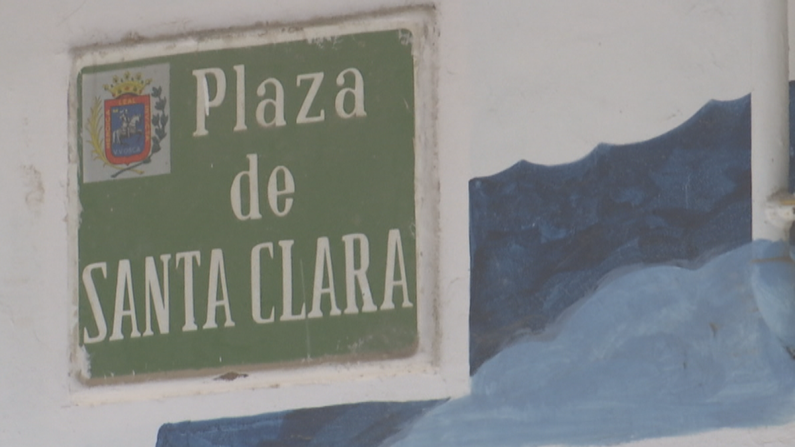 Señal verde con "Plaza de SANTA CLARA" en blanco y escudo heráldico. Mural azul en la pared. Aragón, España.