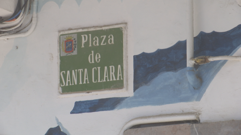 Cartel de calle "Plaza de SANTA CLARA" sobre pared con pintura mural azul y cables eléctricos. Detalle urbano.