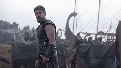 Matt Damon con armadura y barba, empu�a una daga. Al fondo, un campamento con tiendas y barcos antiguos bajo un cielo nublado.