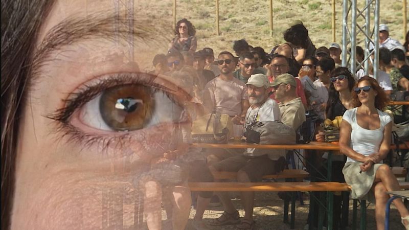 Primer plano de un ojo marrón superpuesto a una multitud al aire libre, con personas sentadas en bancos bajo el sol. Se aprecian detalles de la piel, pestañas y una estructura de celosía.