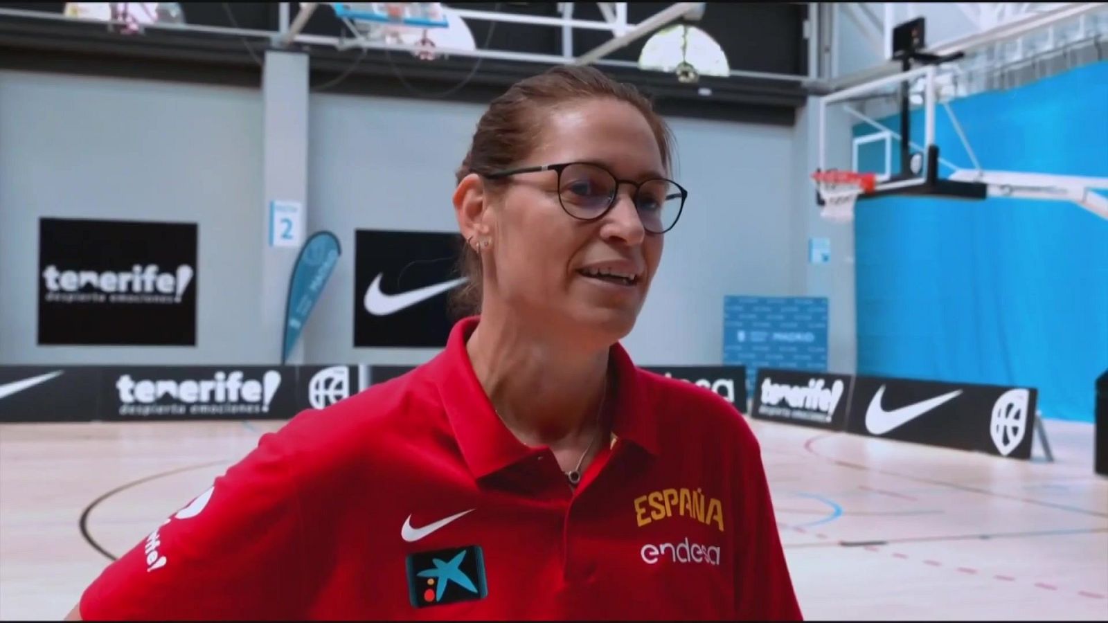 Marta Fernández, comentarista deportiva, posa con un polo rojo, gafas oscuras y una sonrisa. Se aprecian logos de Nike, CaixaBank, "ESPAÑA" y "endesa" en su ropa.