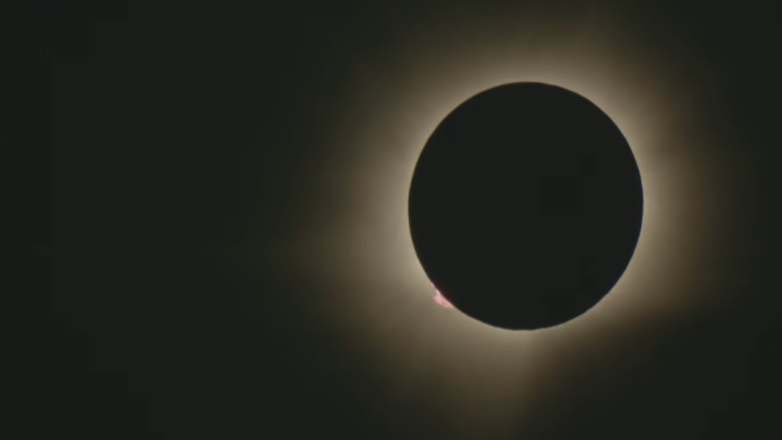 Eclipse solar total con la Luna ocultando el Sol, mostrando la corona solar y una prominencia rojiza. Fondo oscuro.