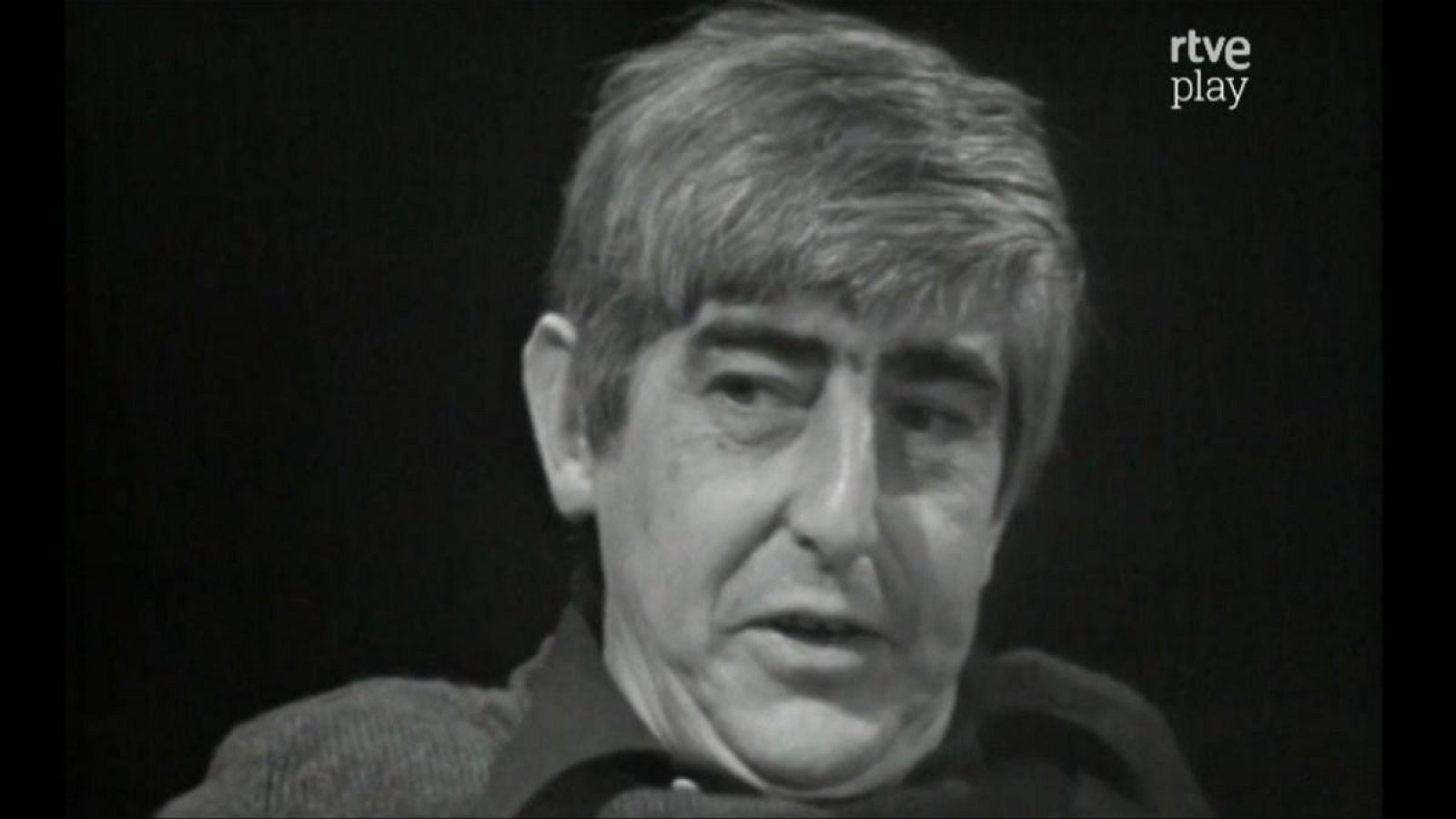 Primer plano en blanco y negro del escritor Juan Benet, con pelo canoso y expresión concentrada. Logo de "rtve play" en la esquina superior derecha.