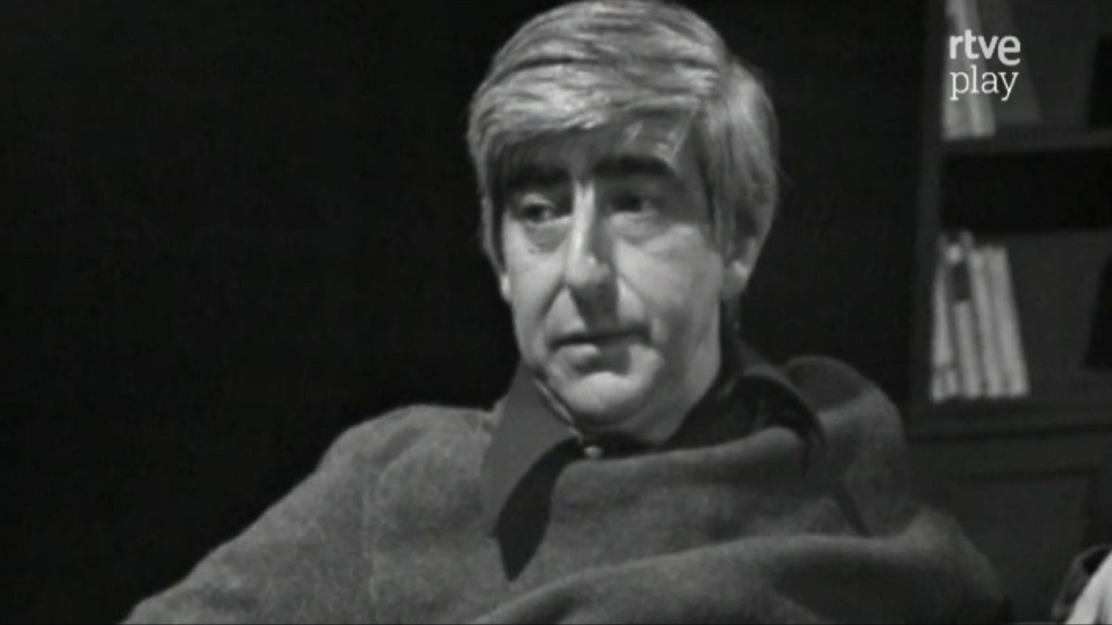 Retrato en blanco y negro de Juan Benet, escritor español, con estantería de libros y logo de rtve play al fondo.