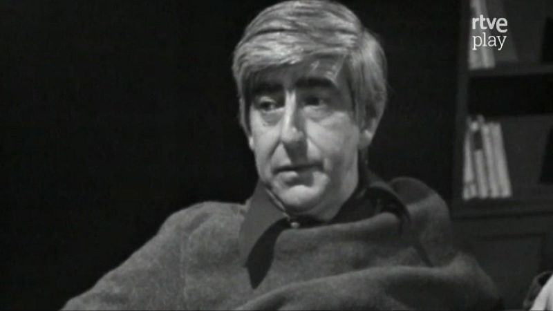 Retrato en blanco y negro de Juan Benet, escritor español, con estantería de libros y logo de rtve play al fondo.
