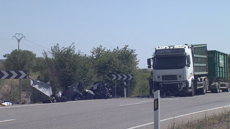 Accidente grave en carretera: camión 'CAMION TROTTER' y coche destrozado. Señal de curva peligrosa y personal de emergencia presentes. Entorno rural con vegetación y torre eléctrica al fondo.
