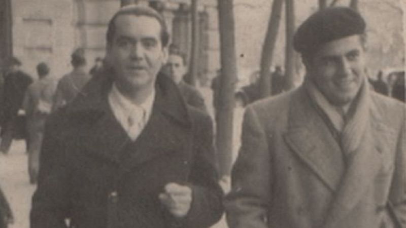 Federico García Lorca y Rafael Rapún, sonriendo mientras caminan juntos al aire libre. Lorca con abrigo oscuro, Rapún con boina y bufanda.