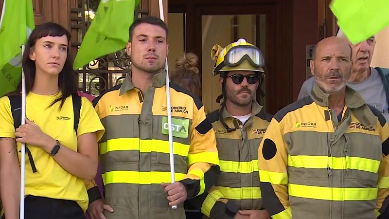 Cuatro trabajadores del "GOBIERNO DE ARAGÓN" y "INFOAR", con uniformes y una bandera verde, posan al aire libre con seriedad.