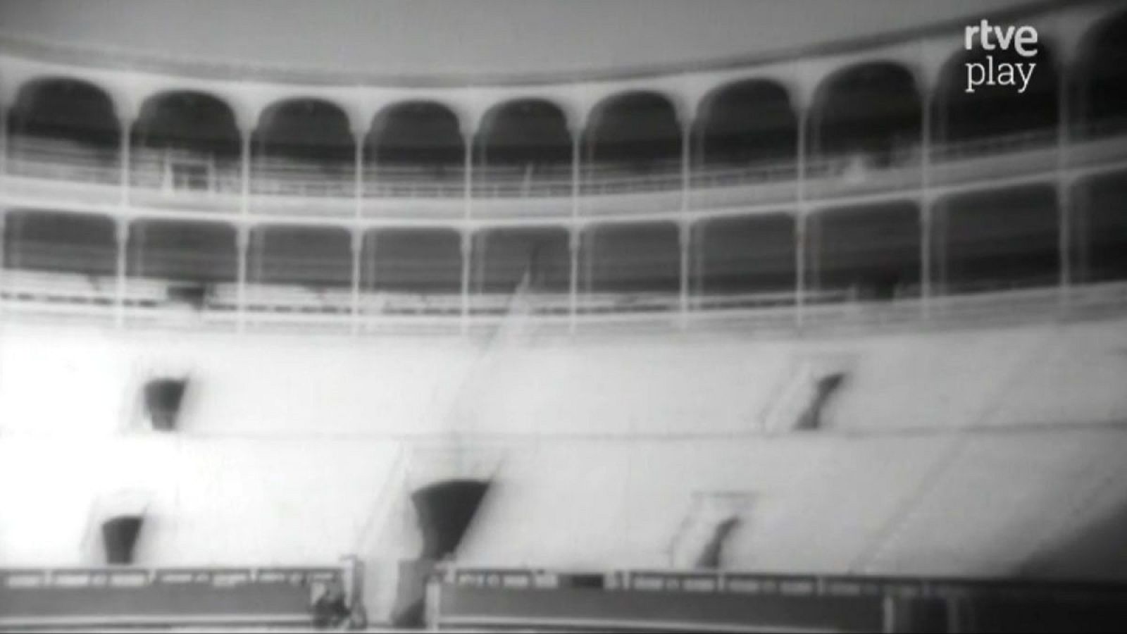 Plaza de toros vacía en blanco y negro, con gradas claras, galerías con arcos oscuros y el logo "rtve play" en la esquina superior derecha.