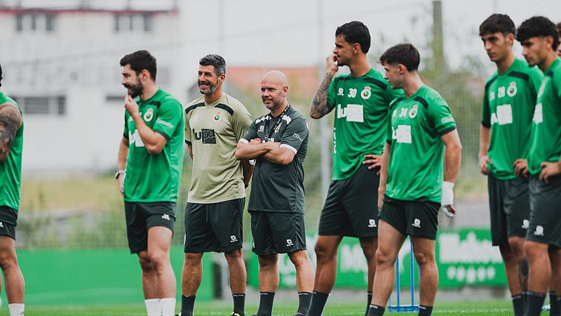 José Alberto López Menéndez, entrenador, con barba y camiseta beige con logo "Lupa", supervisa entrenamiento en campos Nando Yosu junto a cuerpo técnico y jugadores con equipaciones verdes.
