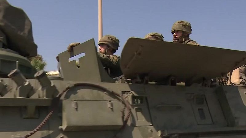 Vehículo militar blindado verde oliva con tres soldados uniformados y cascos. Cielo azul despejado. Operación militar.