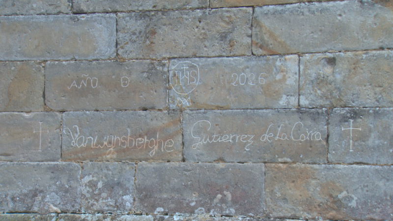 Fachada de piedra con grabados: "AÑO O", "IHS" con cruz, "2026", "Vanwunsberghe", "Gutierrez de la Corra" y cruces.