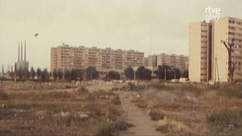Vista panorámica de un paisaje urbano con edificios de apartamentos y una estructura industrial con chimeneas. Se distingue el logo 'rtve play'.