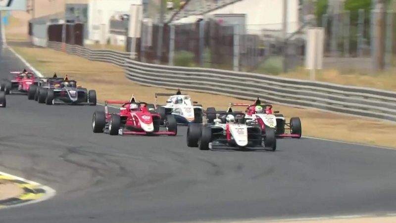 Carrera de automovilismo con coches monoplaza a gran velocidad. Destacan los n�meros "11", "102" y "20" en veh�culos rojos, blancos y azules, compitiendo en un circuito soleado.