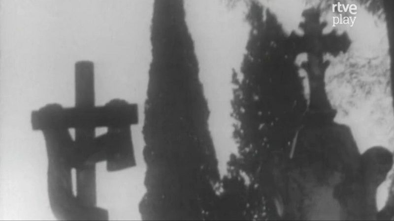 Cementerio en blanco y negro con dos cruces, una simple y otra ornamental, flanqueadas por altos árboles. Logo "rtve play" visible.