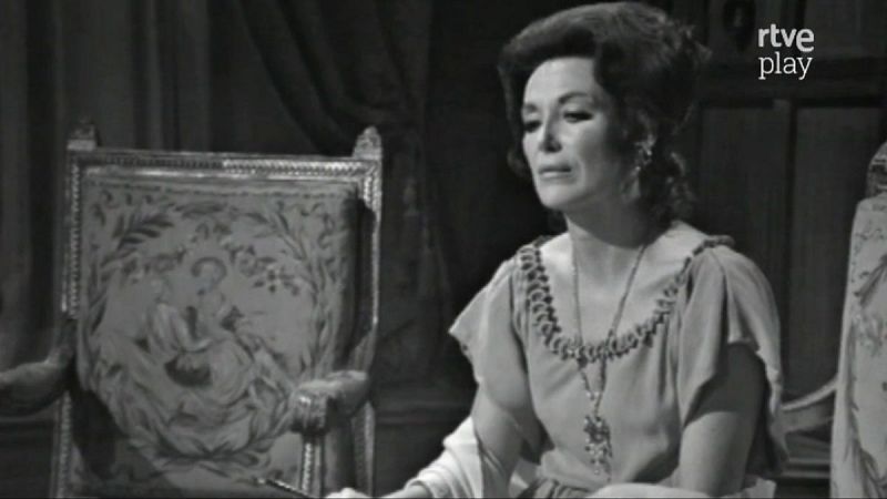 Primer plano de María Asquerino con peinado recogido, vestido y collar, junto a un sillón clásico. Logo de "rtve play" en la esquina superior derecha.
