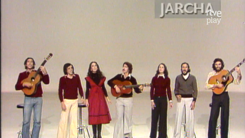 El grupo Jarcha, formado por siete integrantes, canta en un escenario. Dos hombres tocan guitarras acústicas. La imagen muestra el texto "JARCHA" y "rtve play".