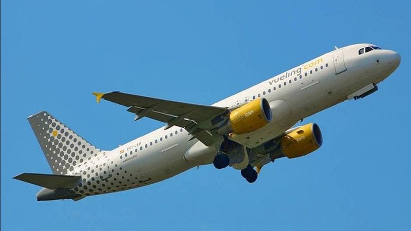 Avión Vueling Airbus A320 EC-JAB en ascenso, cielo azul. "vueling.com" visible en motores. Cola con patrón de puntos.