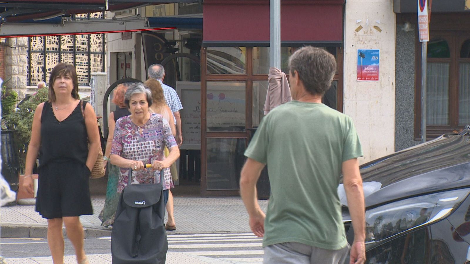 Personas paseando por una calle urbana en Laredo, Cantabria. Se observan edificios, comercios y un coche negro en el fondo.