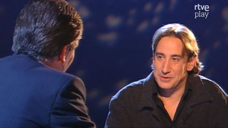 Juanjo Puigcorbé y Pedro Ruiz interactúan en un estudio de televisión, con el logo "rtve play" visible. Puigcorbé, de frente, mira a Ruiz, de espaldas.