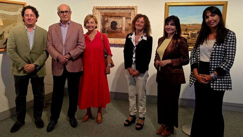 Seis personas posan en una sala de arte con varias obras enmarcadas al fondo. Juan Antonio Pérez Simón, coleccionista de arte, se encuentra entre ellos.