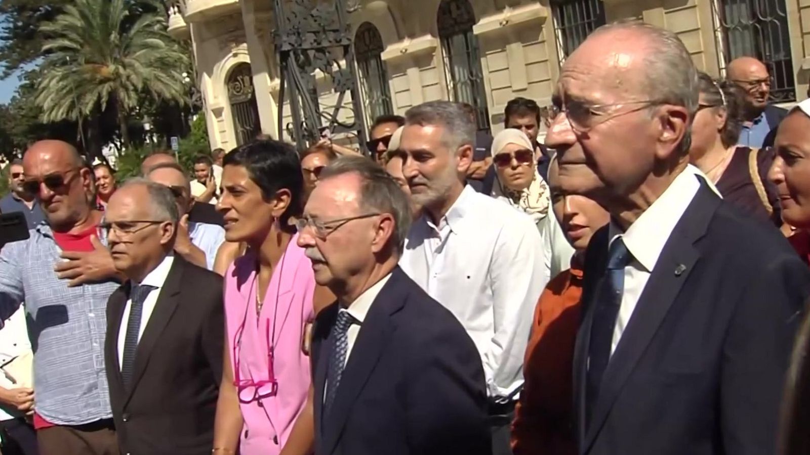 Francisco de la Torre y Juan Vivas, junto a otras personalidades, participan en un acto público en Málaga, con un edificio histórico y palmeras de fondo.