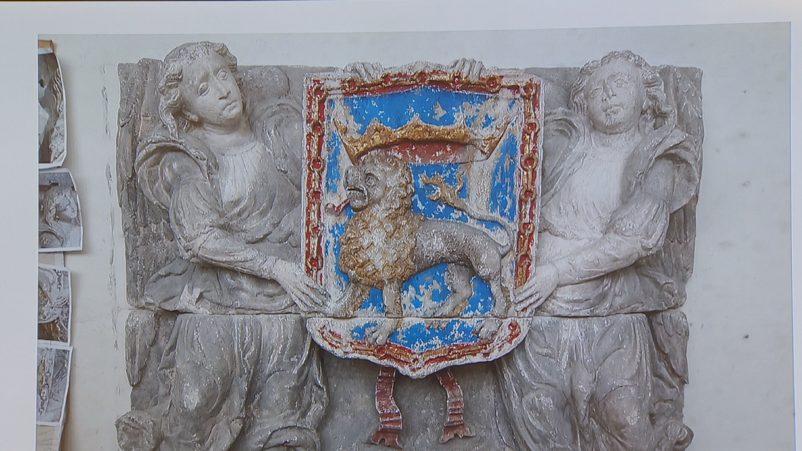 Escultura en relieve del escudo de Pamplona con león rampante coronado, cadenas rojas y figuras alegóricas sosteniéndolo. Realizada en piedra policromada y grisácea.