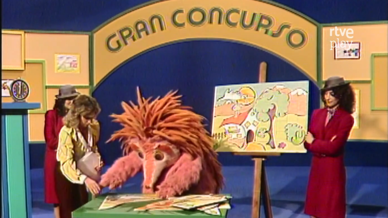 Espinete en un plat� de "GRAN CONCURSO" de "rtve play", interactuando con mujeres y un caballete con una pintura.