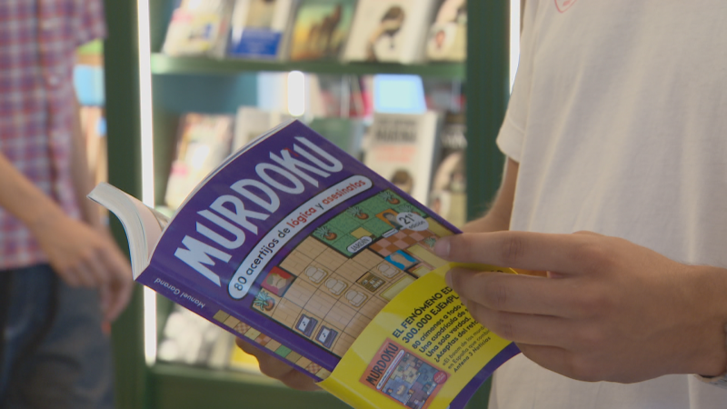 Primer plano de un libro "MURDOKU" con "80 acertijos de lógica y asesinatos" de Manuel Durand, promocionado como "fenómeno" con 300.000 ejemplares y mención en Antena 3 Noticias.