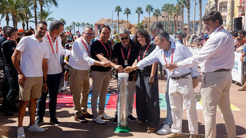 Alejandro Valverde participa en un sorteo o acto ceremonial en la Costa Blanca, introduciendo objetos en una urna junto a otras personas.