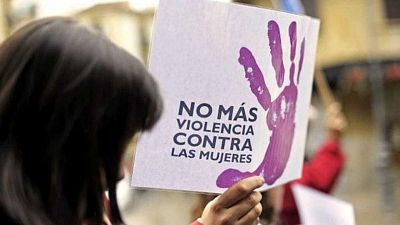 Primer plano de un cartel "NO M�S VIOLENCIA CONTRA LAS MUJERES" con huella de mano morada, sostenido por una persona en una manifestaci�n.