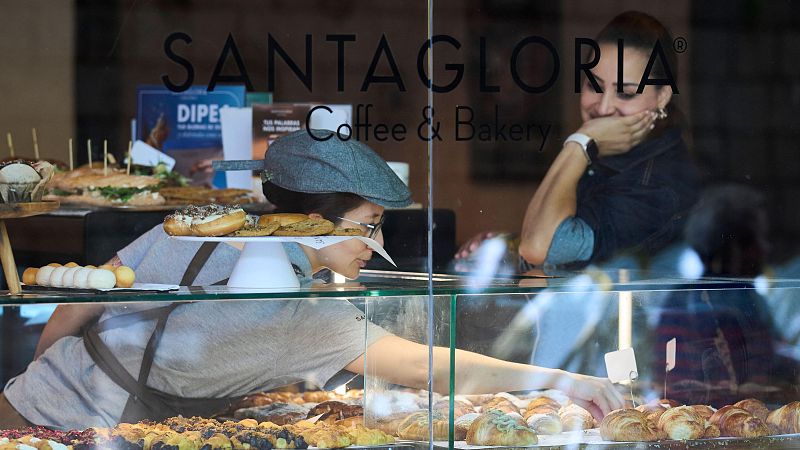 Tamara Falcó sonríe mientras observa a una trabajadora organizar bollería en la vitrina de una pastelería.