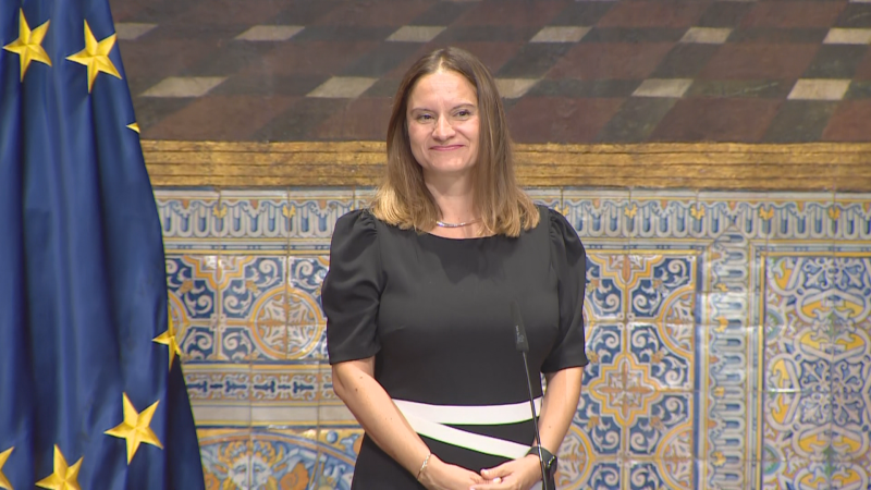Aitana Ferrer, presentadora de "L'informatiu - Comunitat Valenciana", posa con un vestido negro y blanco, ante azulejos valencianos y la bandera de la UE.
