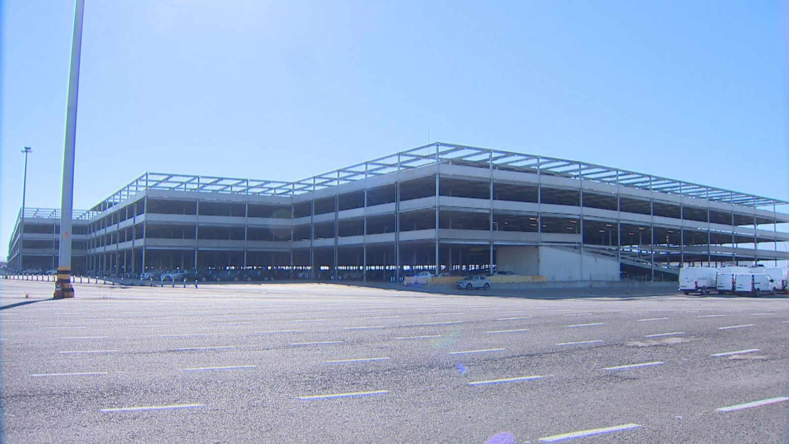 Gran silo vertical de automóviles en construcción en el Puerto de Santander, con vehículos estacionados y furgonetas blancas en la explanada.