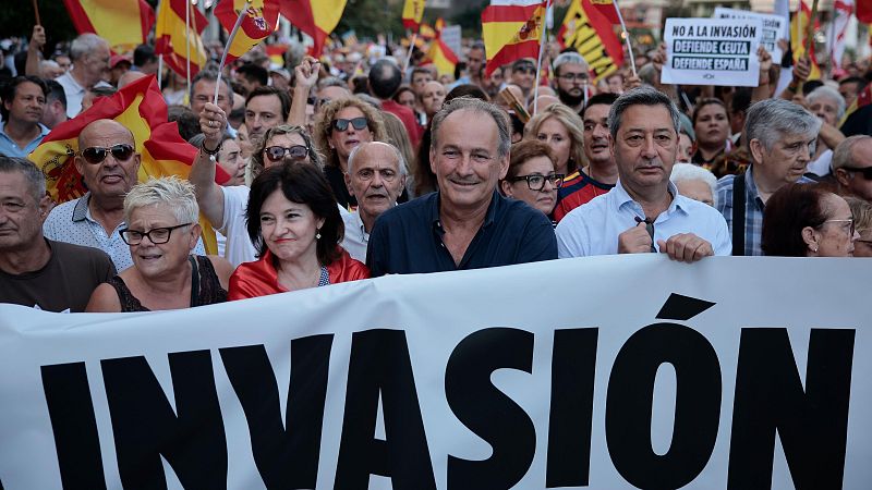 Manifestación con José María Aznar y Santiago Abascal portando pancarta "INVASIÓN". Multitud con banderas de España y cartel "NO A LA INVASIÓN".