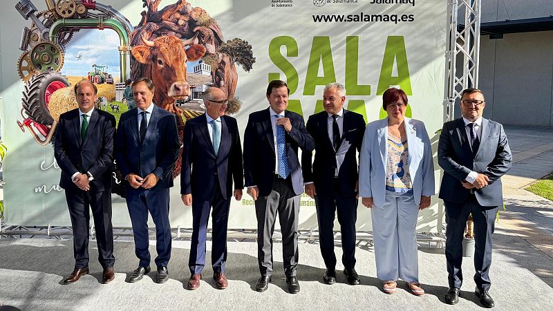 Grupo de siete personas, incluyendo a Alfonso Fernández Mañueco, posan frente a un panel de Salamaq con temática agrícola y ganadera.