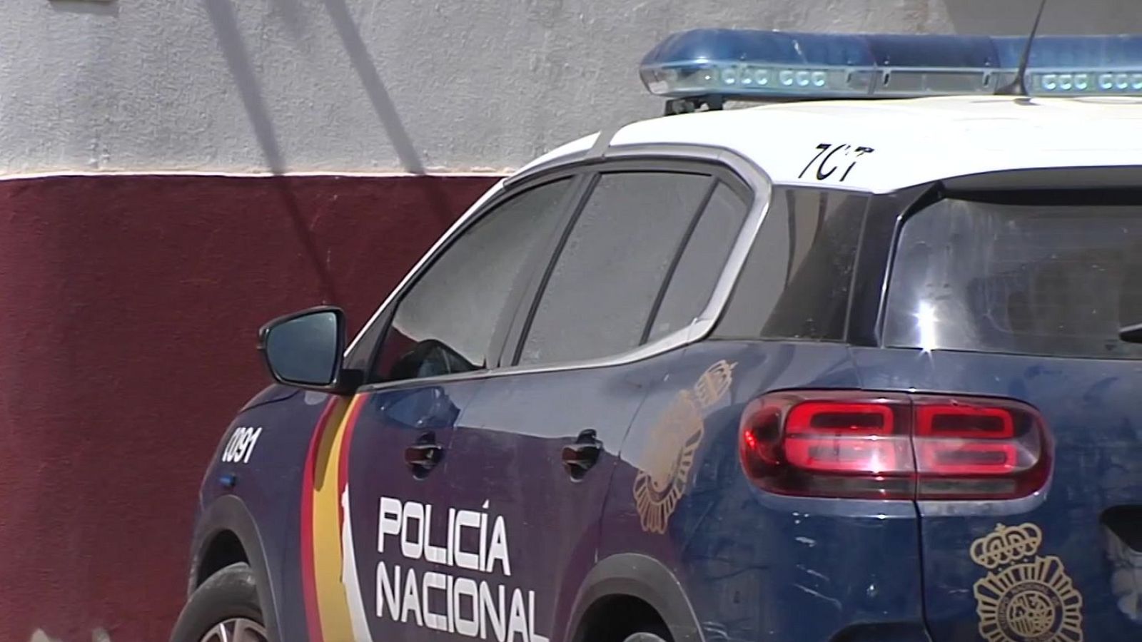 Vehículo policial de la Policía Nacional de España, SUV azul oscuro con techo blanco, franjas rojas y amarillas, "POLICÍA NACIONAL", "091", "7C7", rotativo azul, escudo oficial.