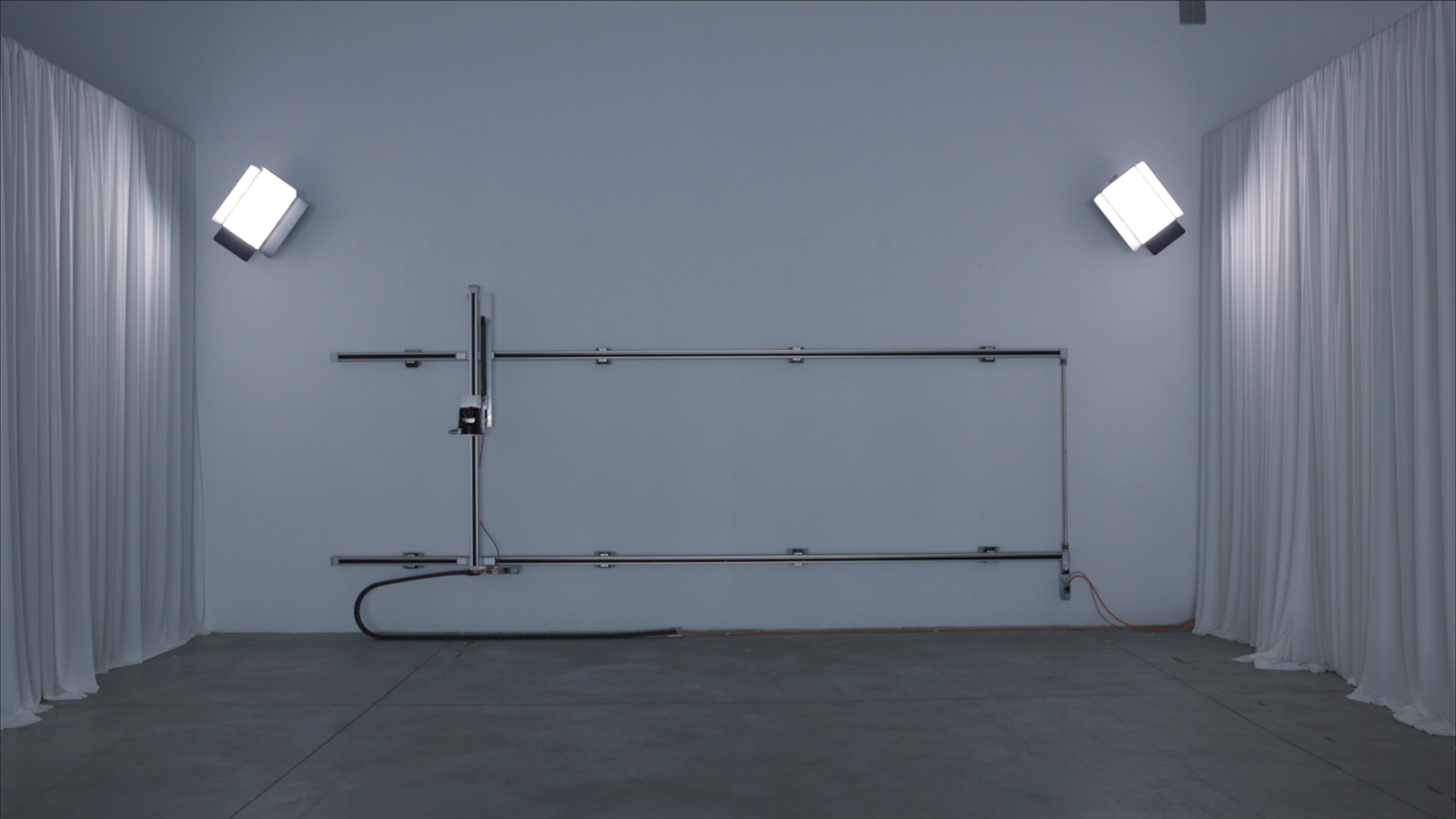 Habitaci�n moderna con paredes grises, suelo de hormig�n, focos, estructura met�lica y cortinas blancas. Un cable negro y otro rojizo son visibles.