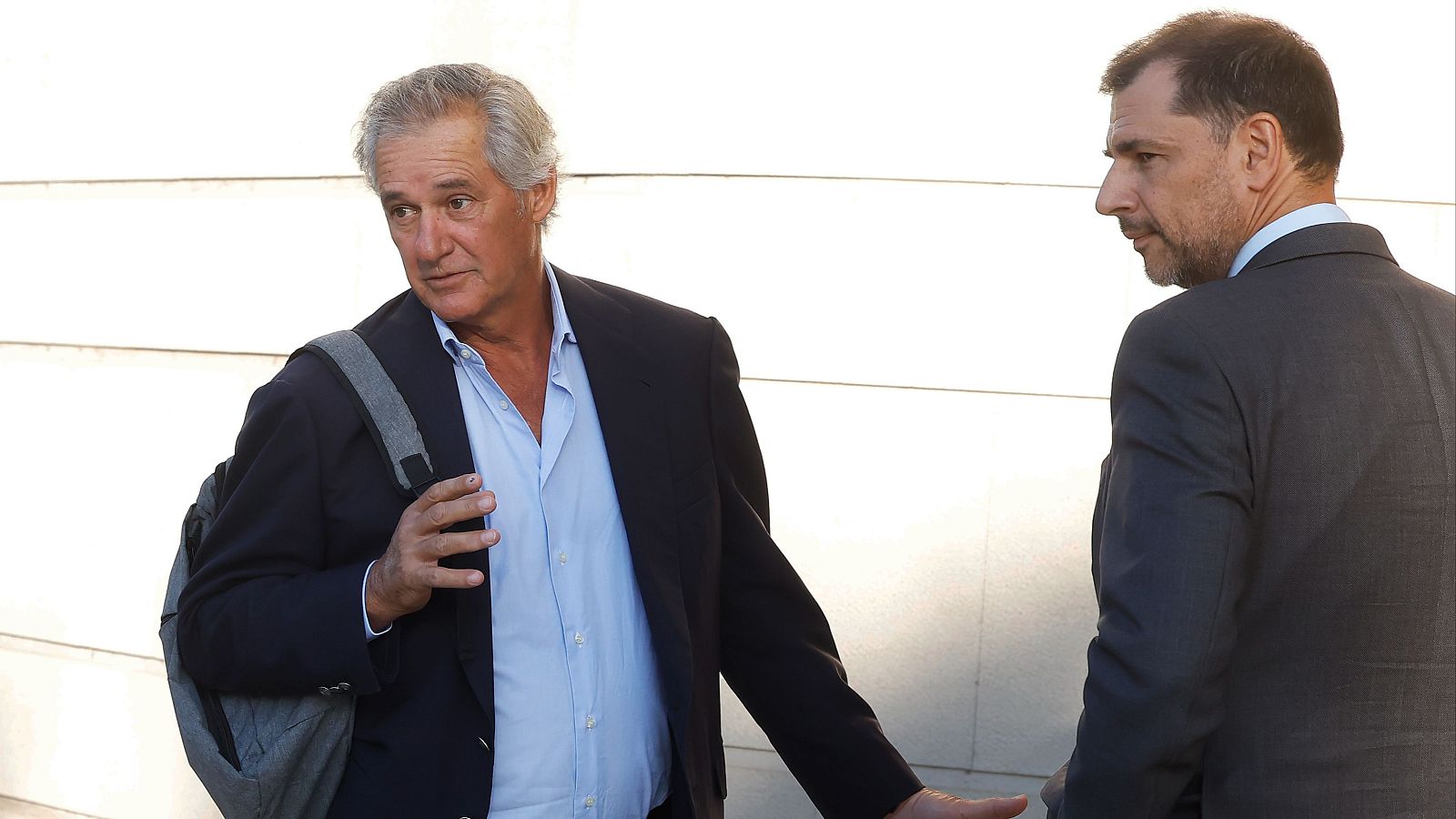 José Manuel Entrecanales Domecq, con cabello canoso y traje azul marino, camina en un exterior de edificio en Pamplona, acompañado por un hombre de perfil con traje oscuro. Ambos miran en la misma dirección.