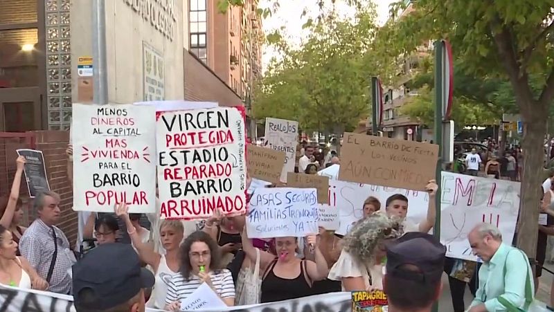 Manifestación urbana con pancartas exigiendo vivienda digna y criticando la inversión de capital. "MENOS DINERO AL CAPITAL MAS VIVIENDA PARA EL BARRIO POPULAR", "REALOJOS URGENTES", "CASAS SEGURAS FAMILIAS TRANQUILAS".